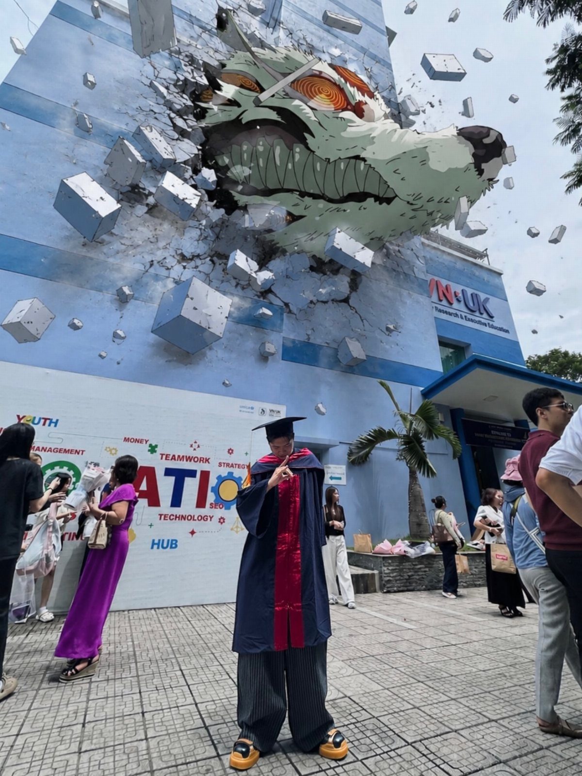 Graduate in gown posing before a giant wolf sculpture breaking through a building