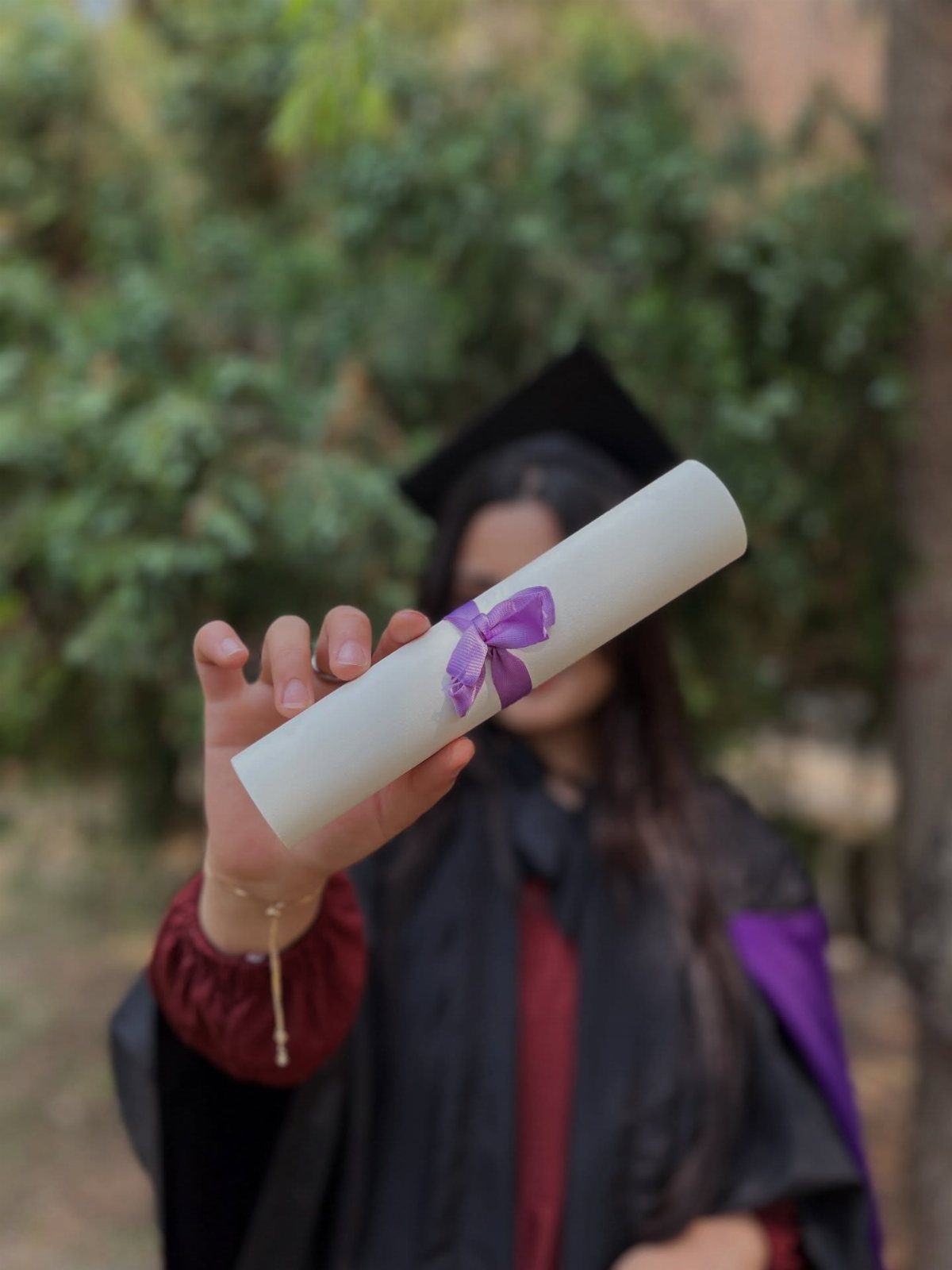 Graduation diploma tied with purple ribbon held forward by a graduate in gown