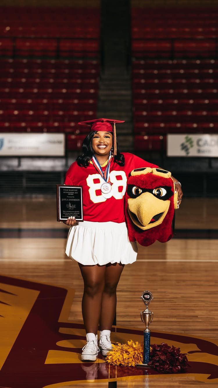Graduating woman in red jersey holding a plaque and a red bird mascot head.