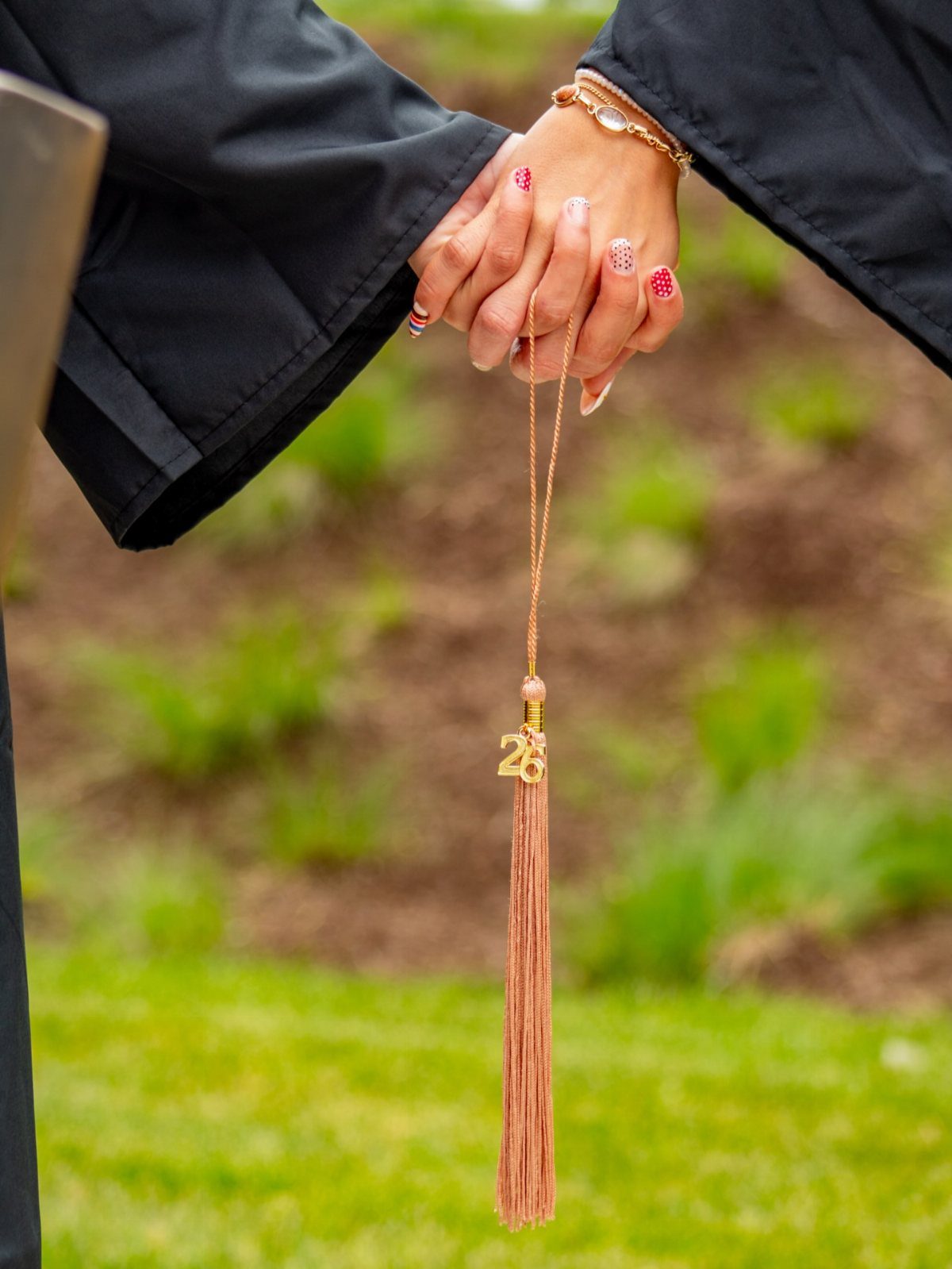 Hand in black graduation gown holding a gold tassel with number 26