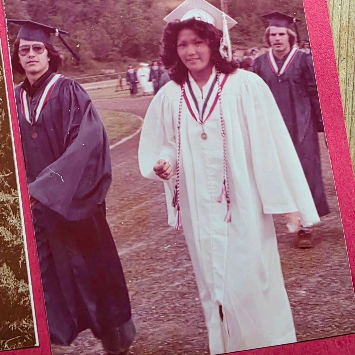 Graduates in white and blue gowns walking outdoors in a vintage photograph.