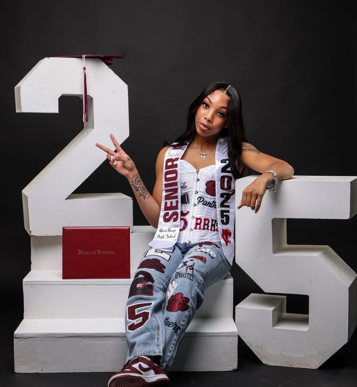 Young woman in school colors posing with large white numbers 25 for graduation.