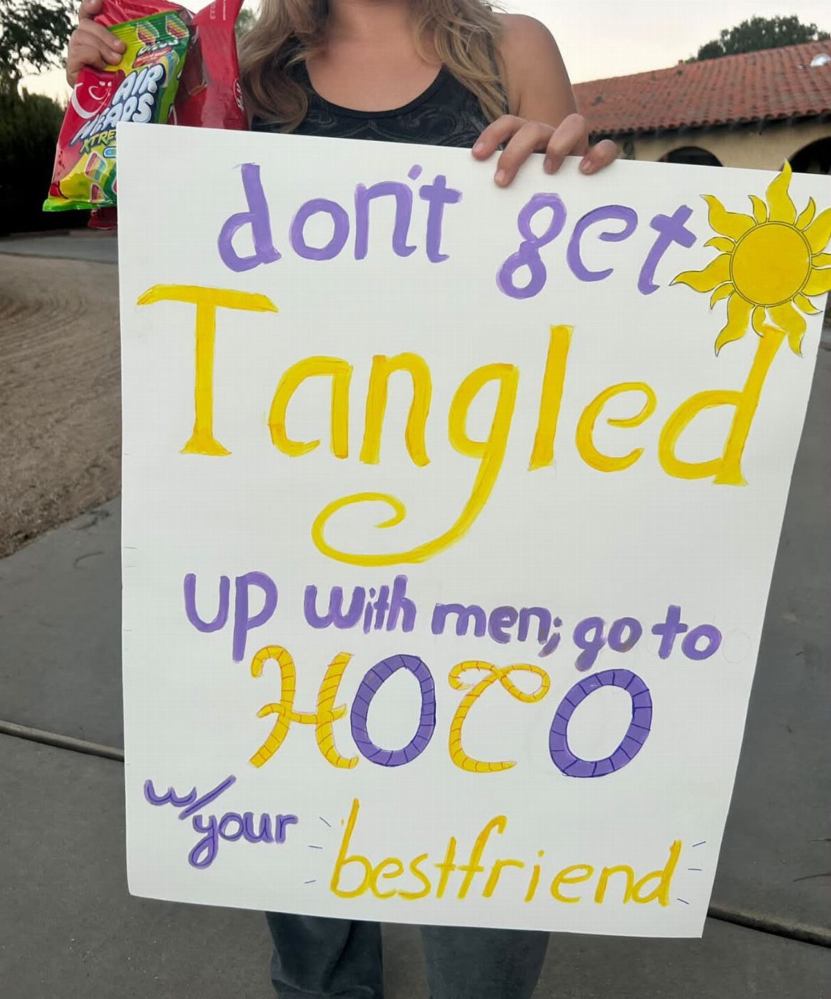Hand-drawn hoco proposal poster with purple and yellow text held by a person.