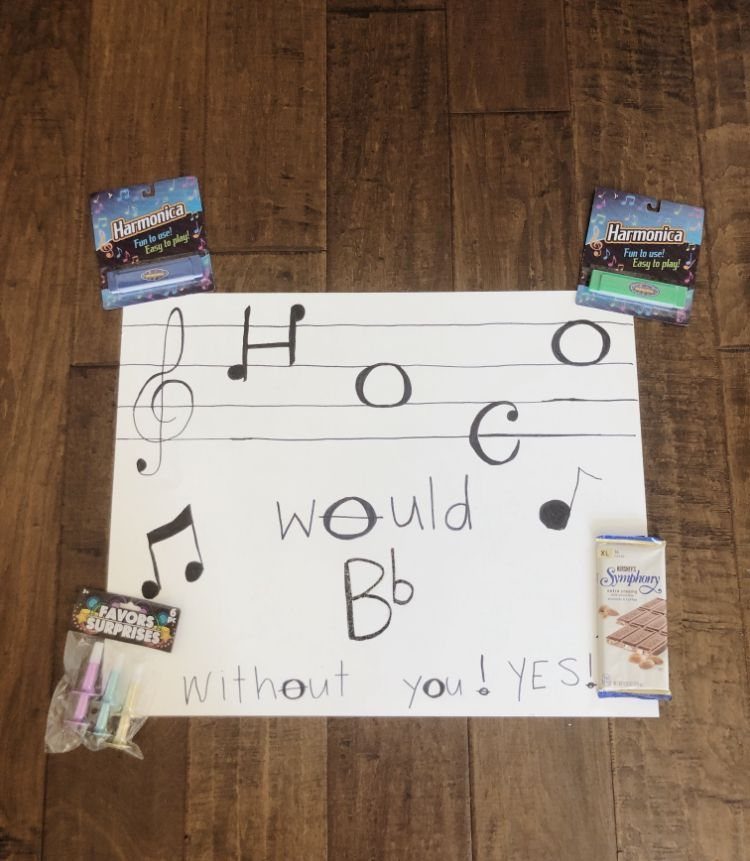 Music themed homecoming proposal poster with harmonicas and a chocolate bar on wood.
