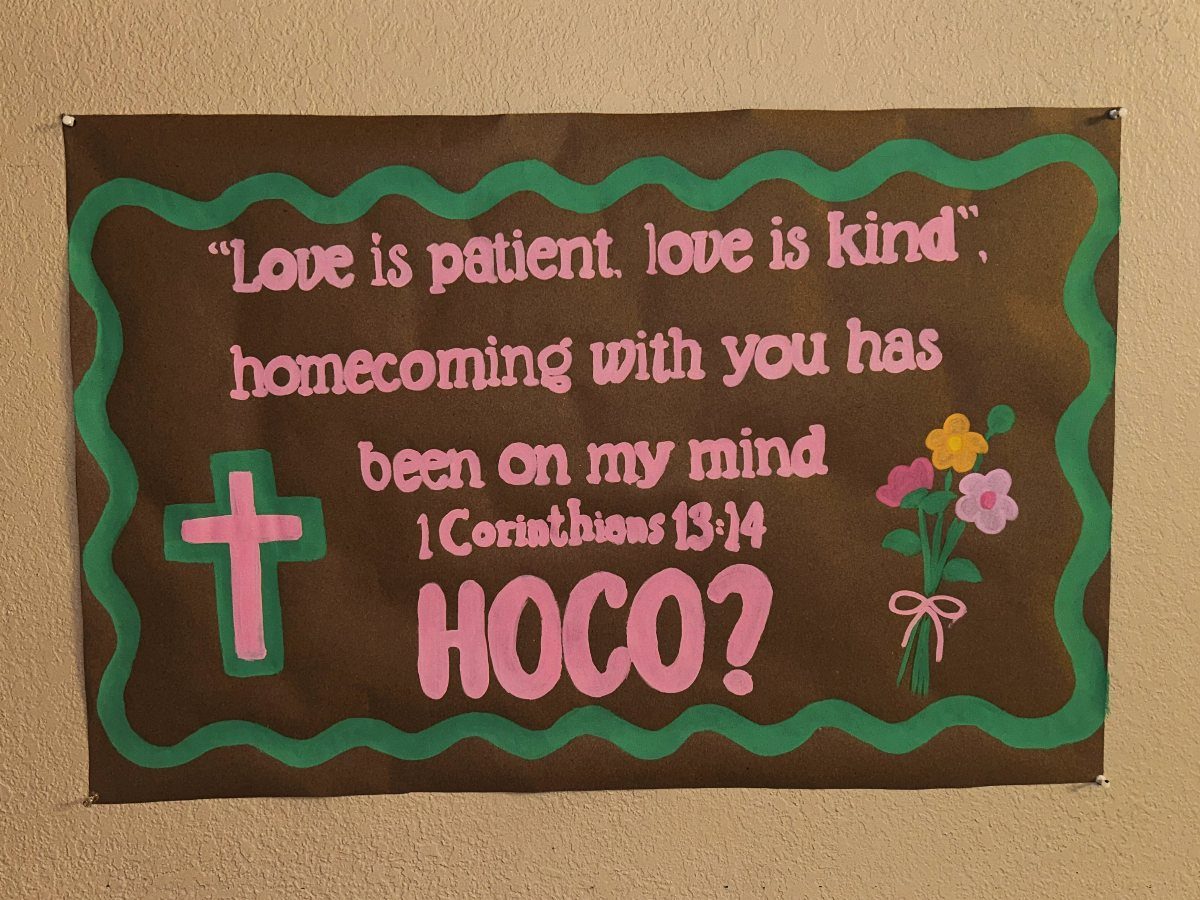 Brown homecoming proposal poster with pink text, a cross, and small flowers.