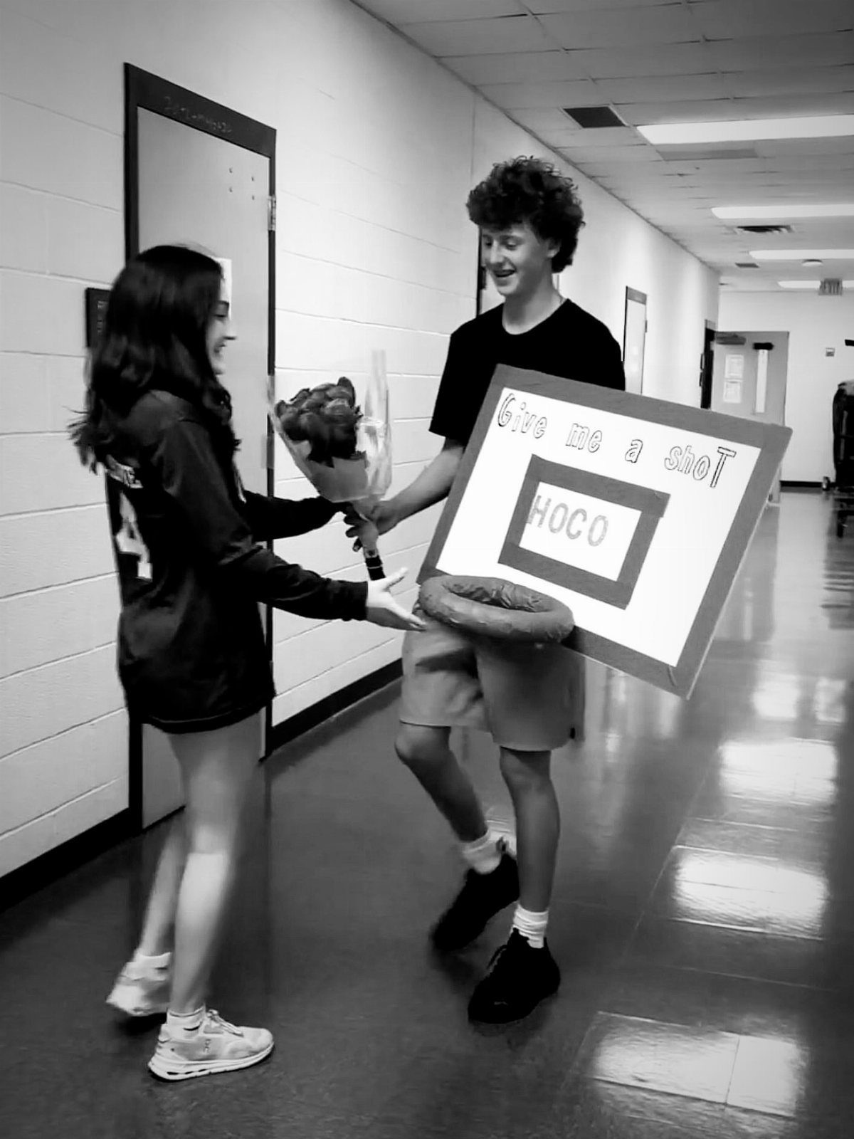 Teenage boy holding a basketball themed homecoming proposal poster for a teenage girl.