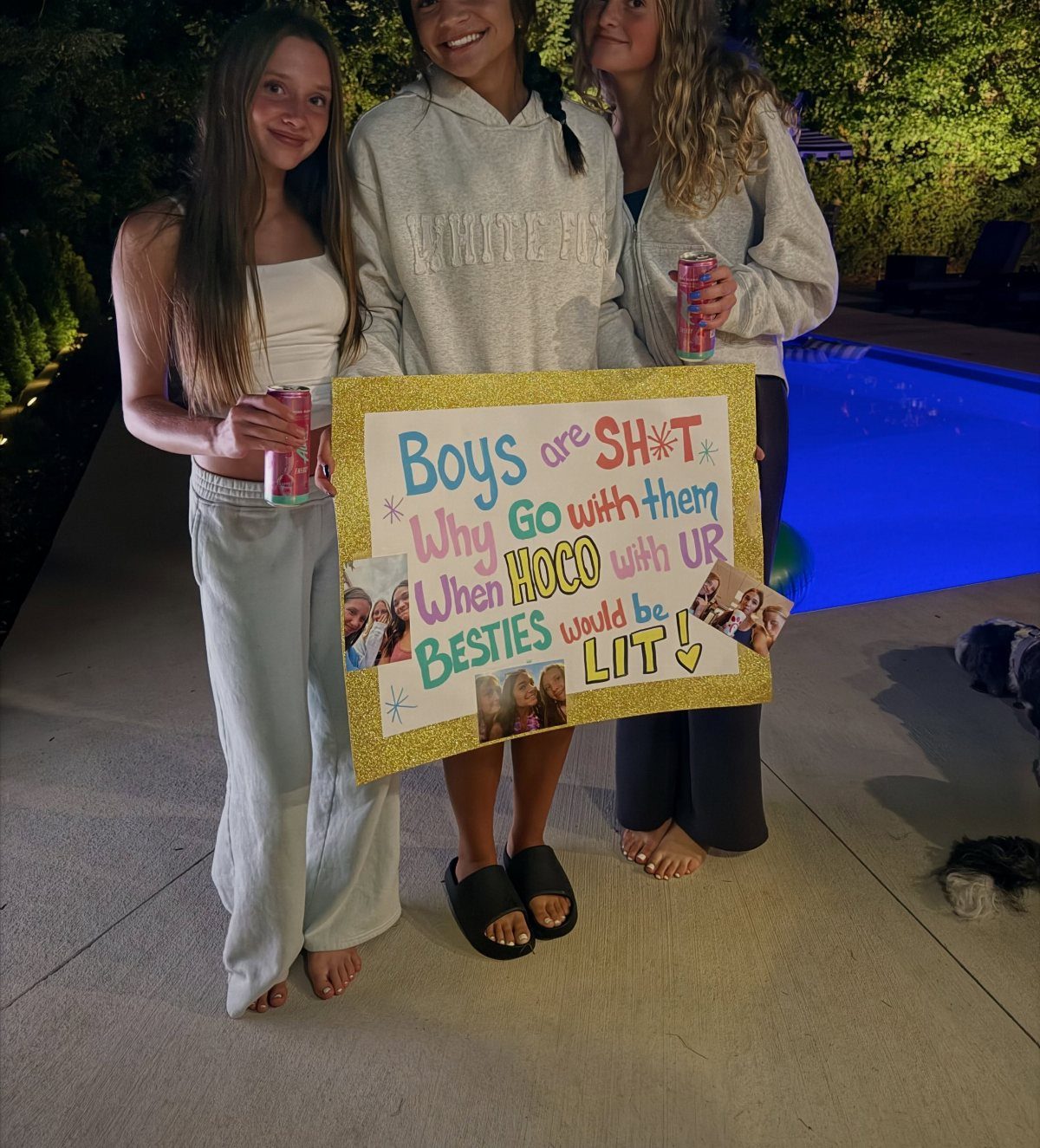 Three teenage girls holding a glittery homecoming proposal poster for their group of friends.