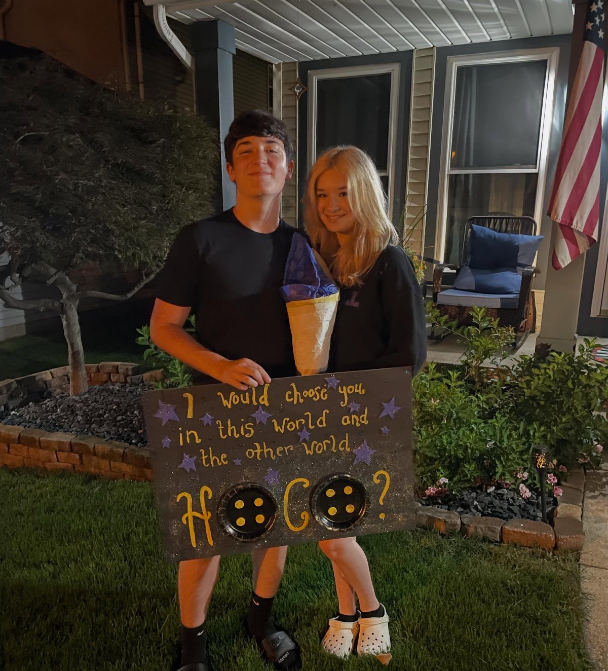 Teenage couple posing with a black homecoming proposal poster featuring a movie quote.