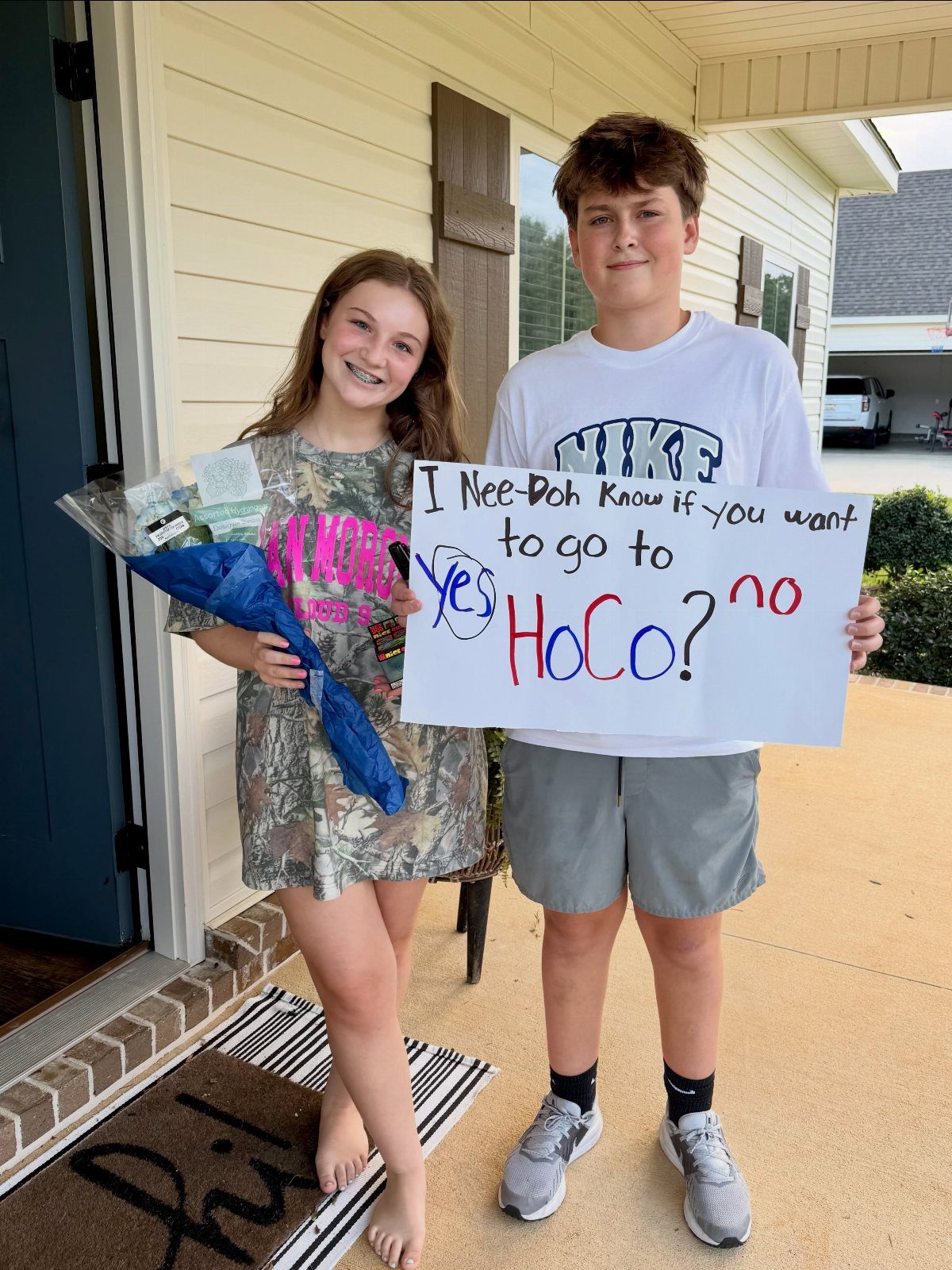 Teenage boy holding a homecoming proposal poster while standing with a teenage girl.