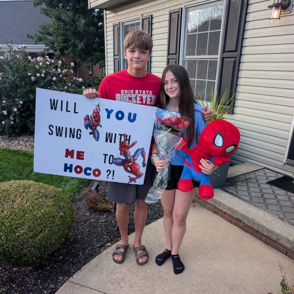 Teenage couple posing with a Spider-Man themed homecoming proposal poster and plush toy