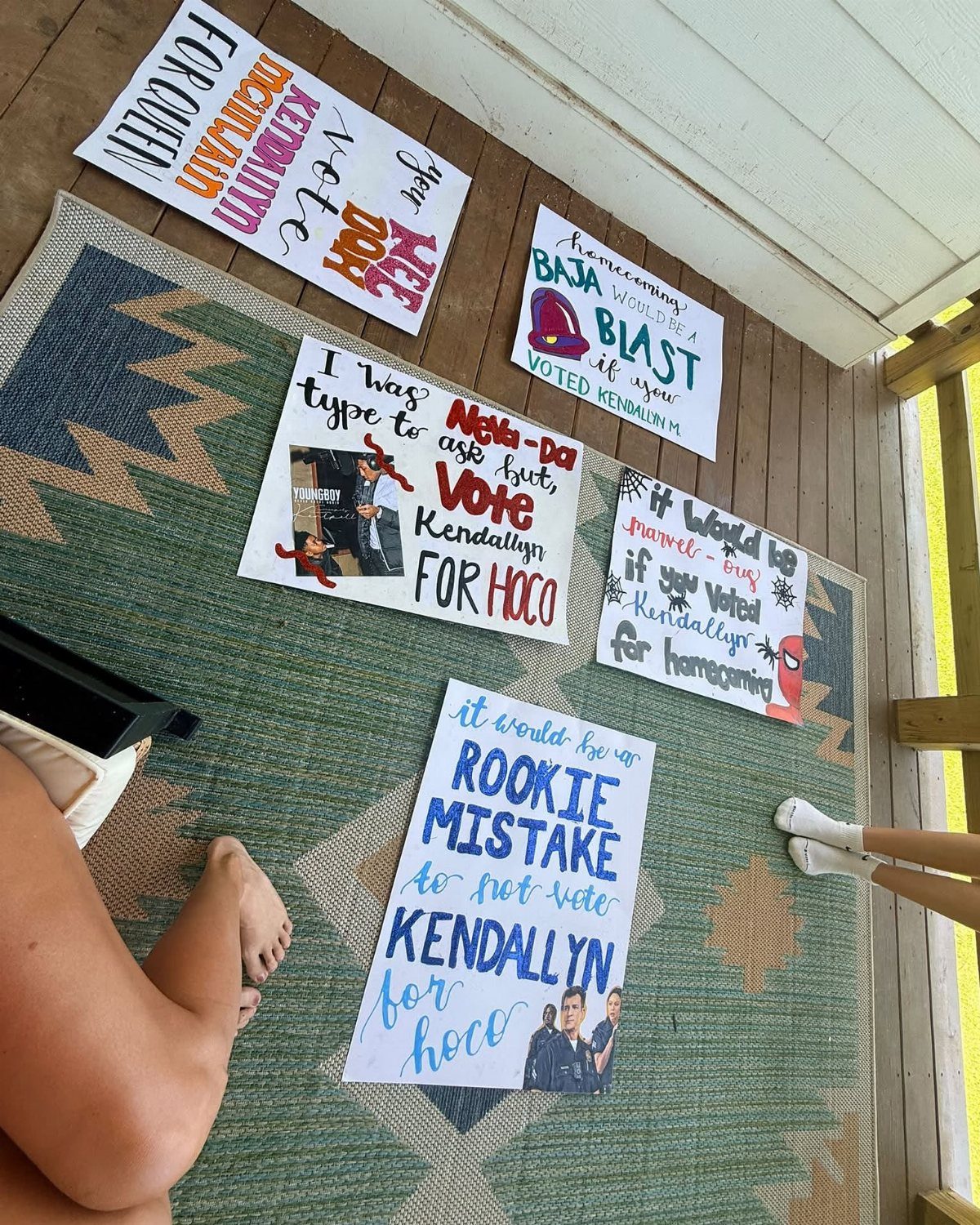 Handmade homecoming court campaign posters with colorful lettering lying on a patterned rug.
