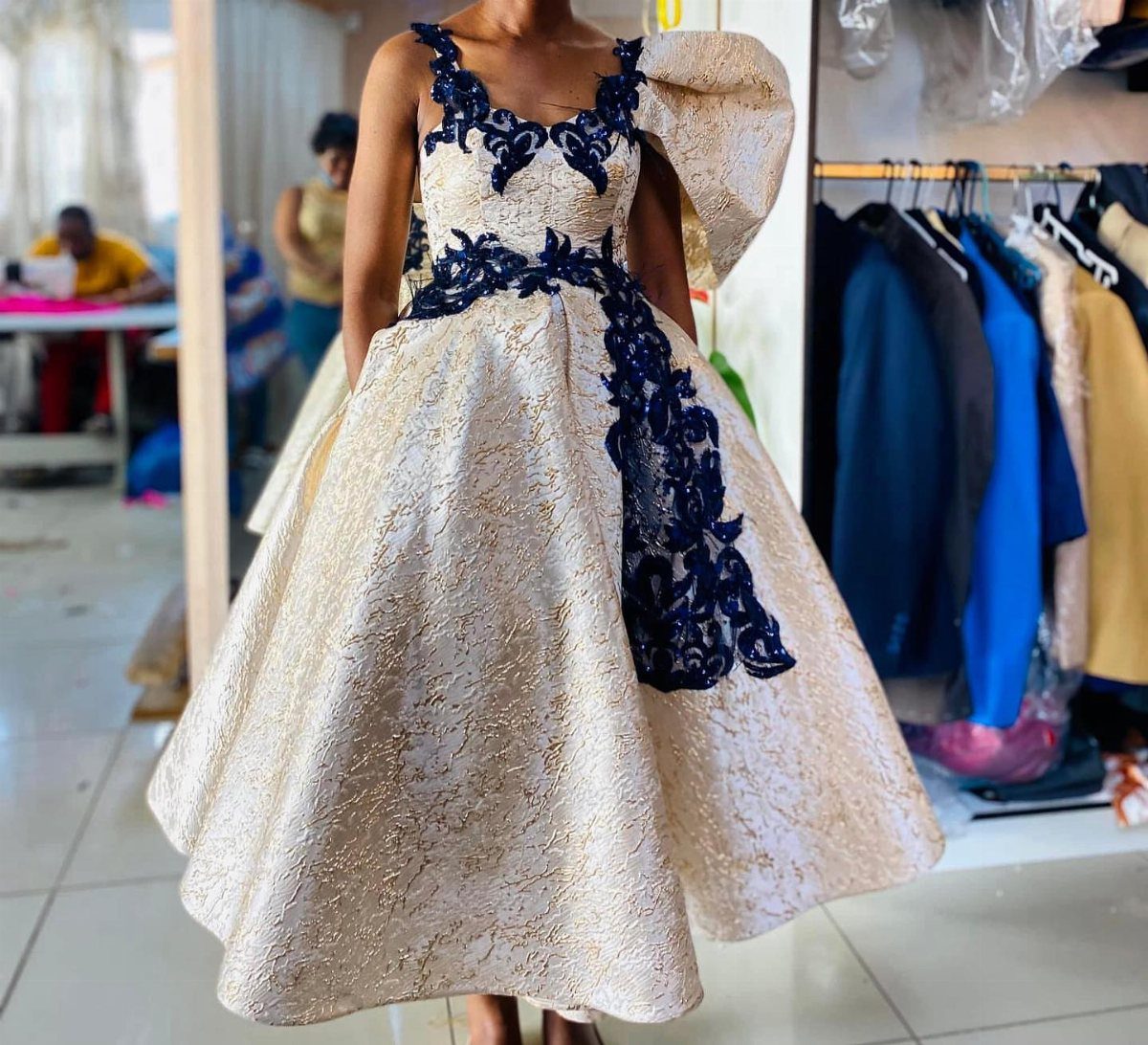 Cream brocade tea-length dress with navy blue lace floral accents and one puff sleeve.