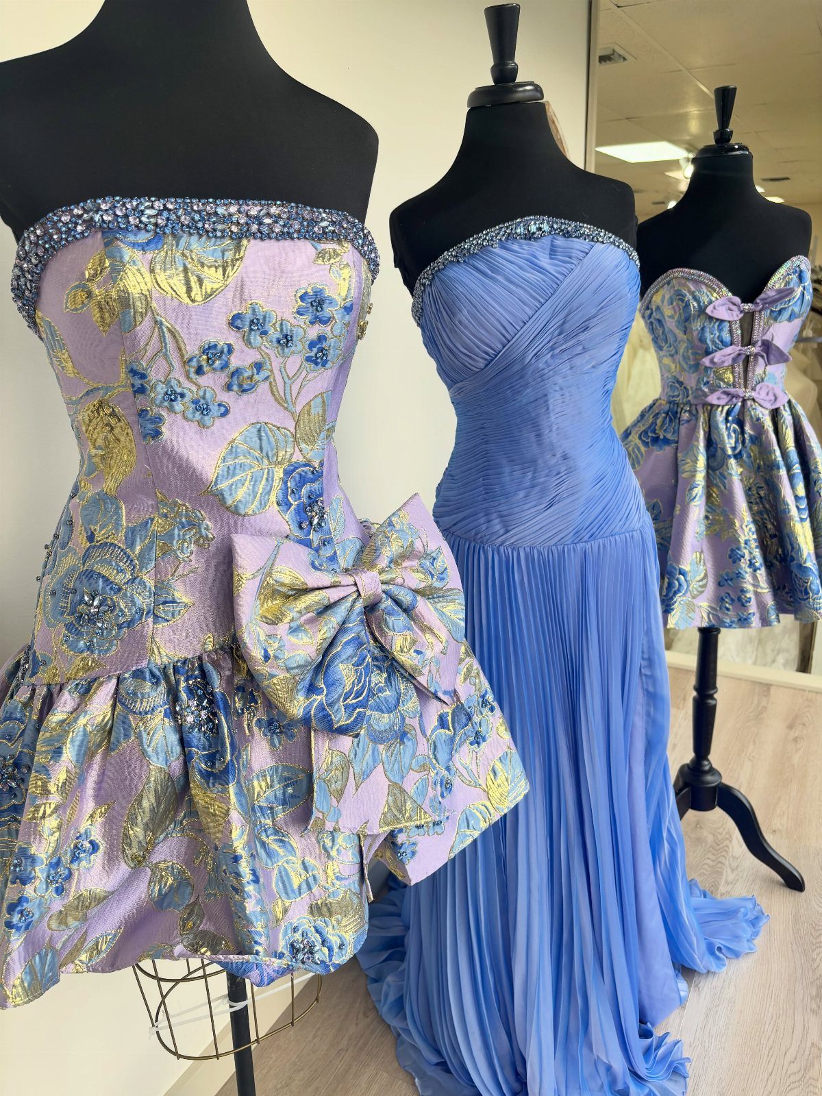Floral print purple homecoming dresses and a long blue gown on mannequins.