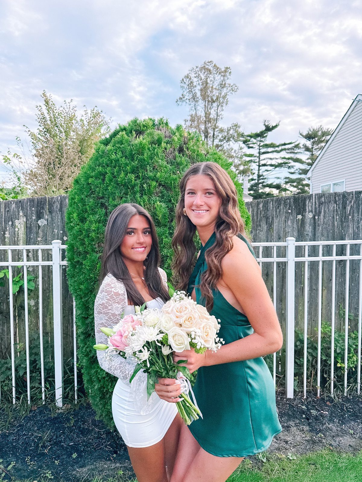 Two young women in short white and green party dresses holding a flower bouquet.