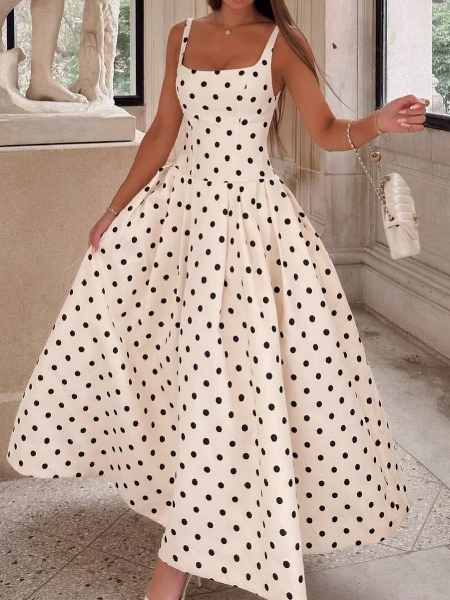 Woman wearing a white floor-length polka dot dress and holding a white handbag.