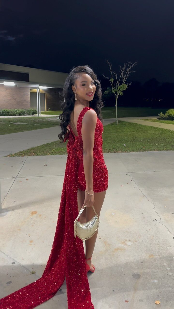 Woman in a sparkling red sequined dress with a long train and gold handbag.