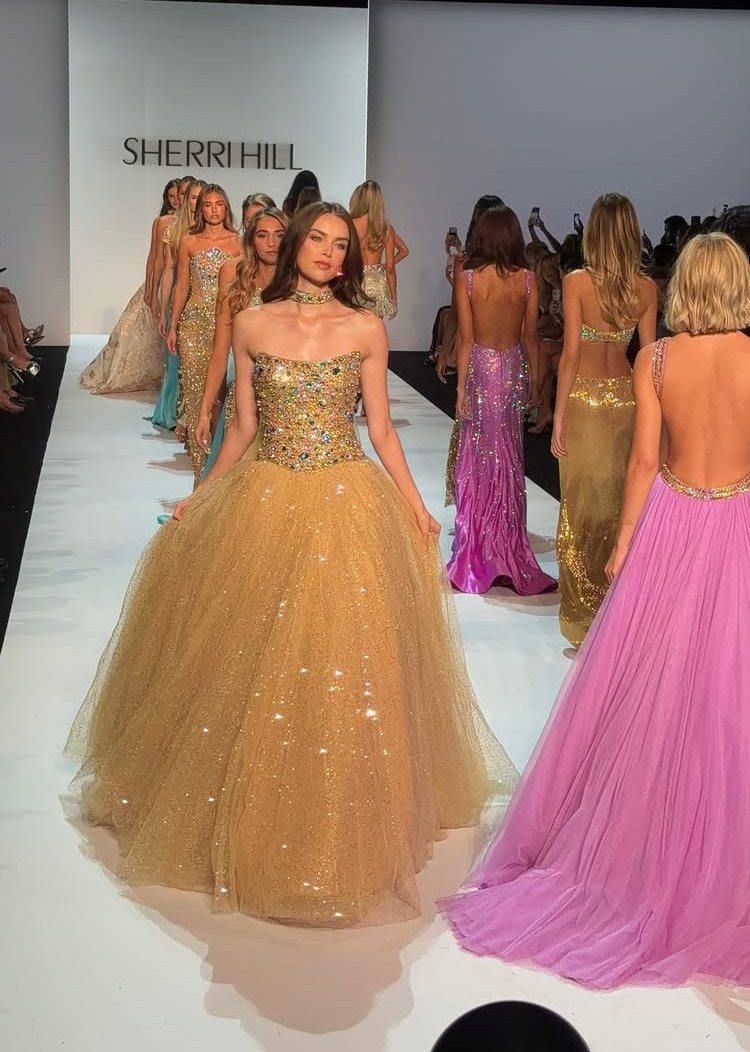 Models on a runway wearing long, sparkling gold and purple formal homecoming dresses.