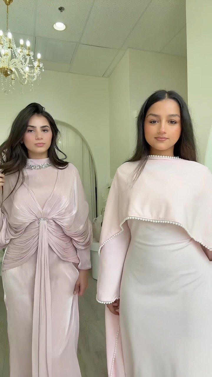 Two women wearing modest, long light pink formal gowns in a bright room.