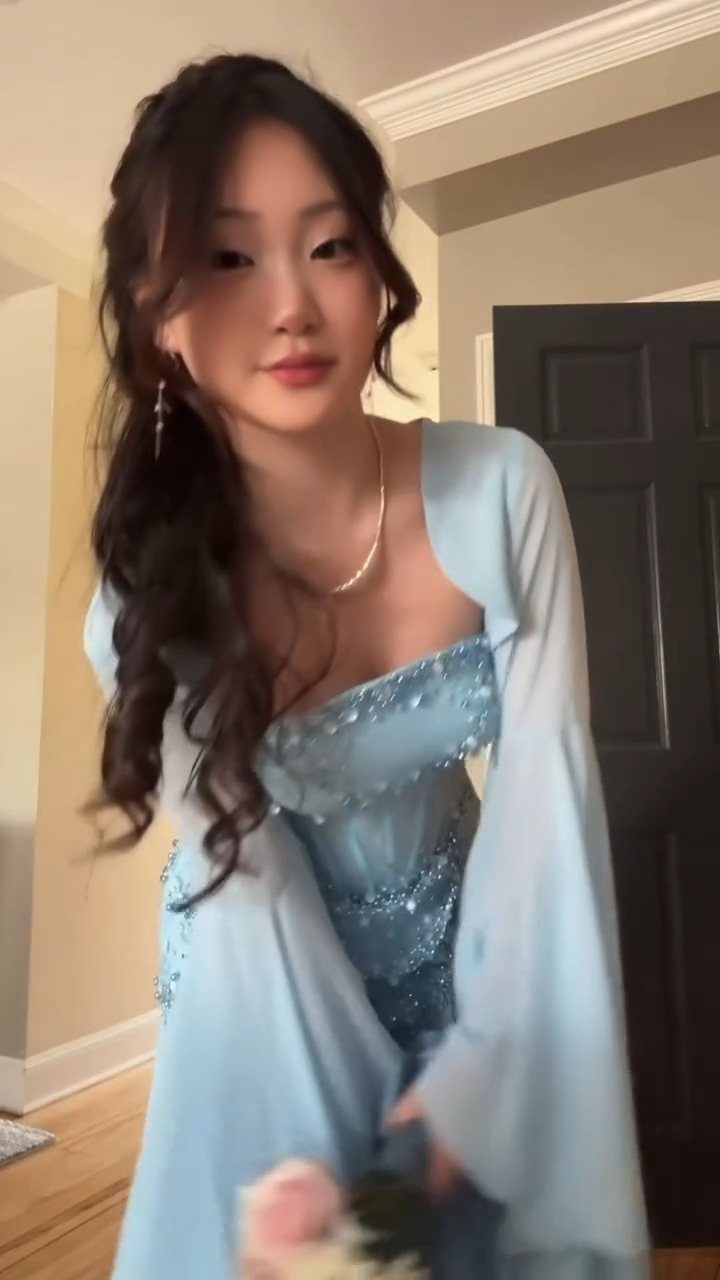 Young woman wearing a light blue sequined dress and matching robe indoors.