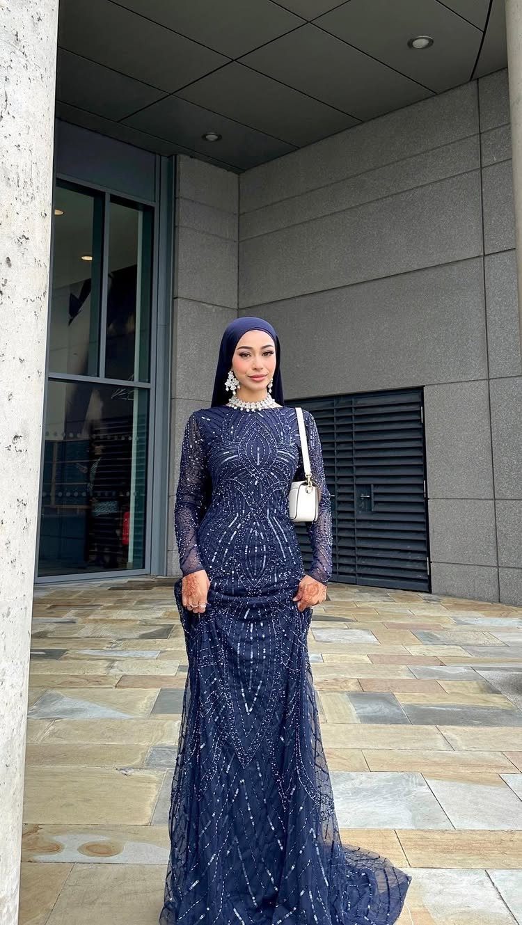 Woman in a modest navy blue sequined gown and hijab standing outdoors.