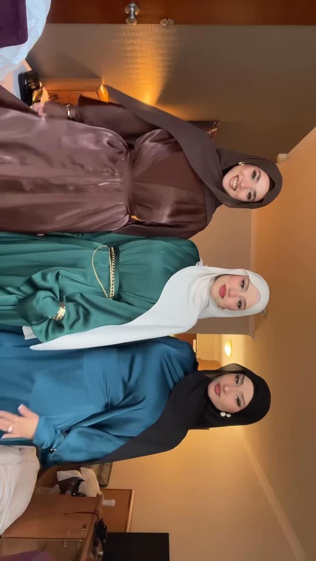 Three women wearing modest long-sleeved satin gowns and hijabs in brown, green, and blue.