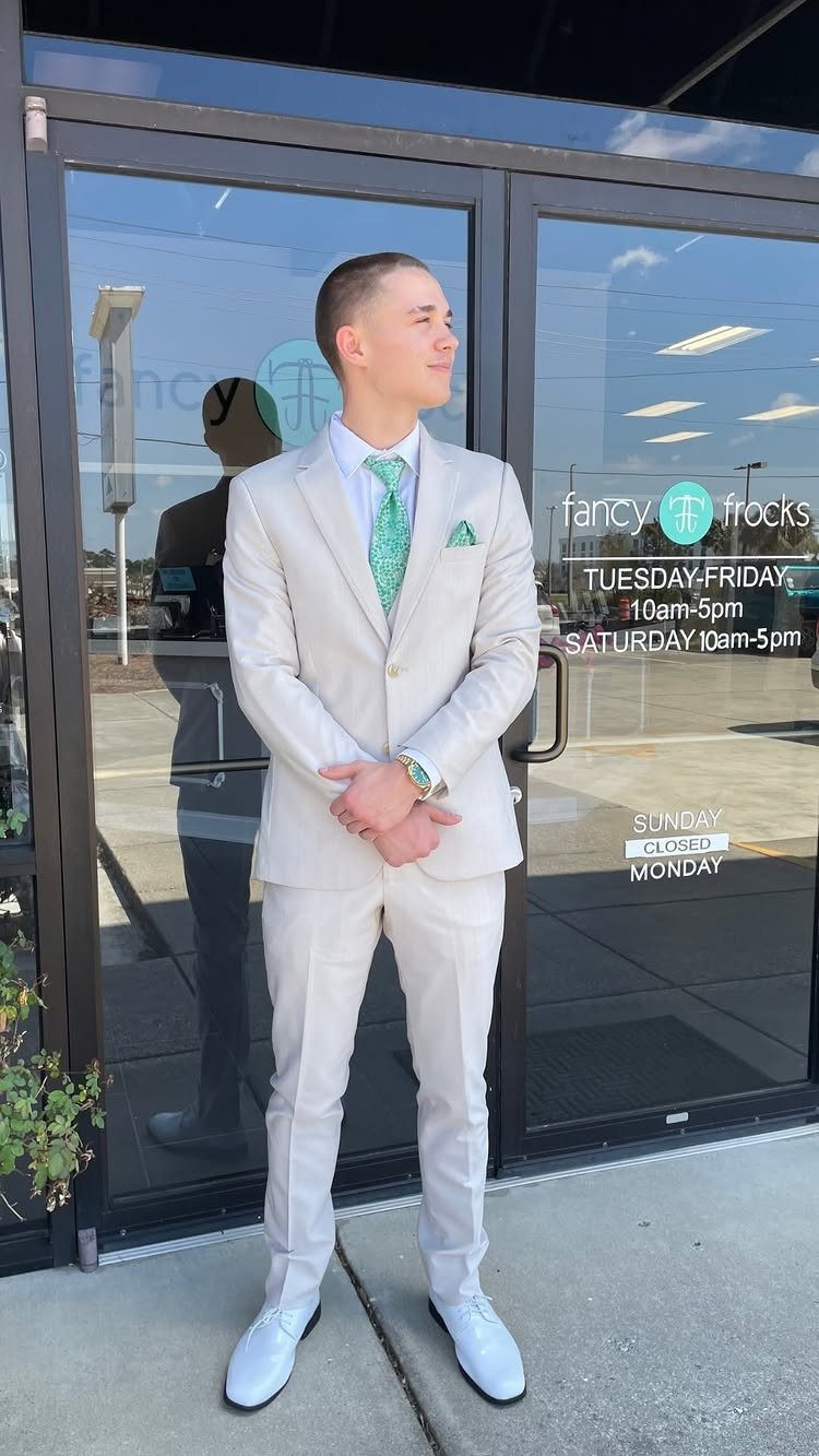 Young man wearing a light beige suit with a green tie and white shoes.