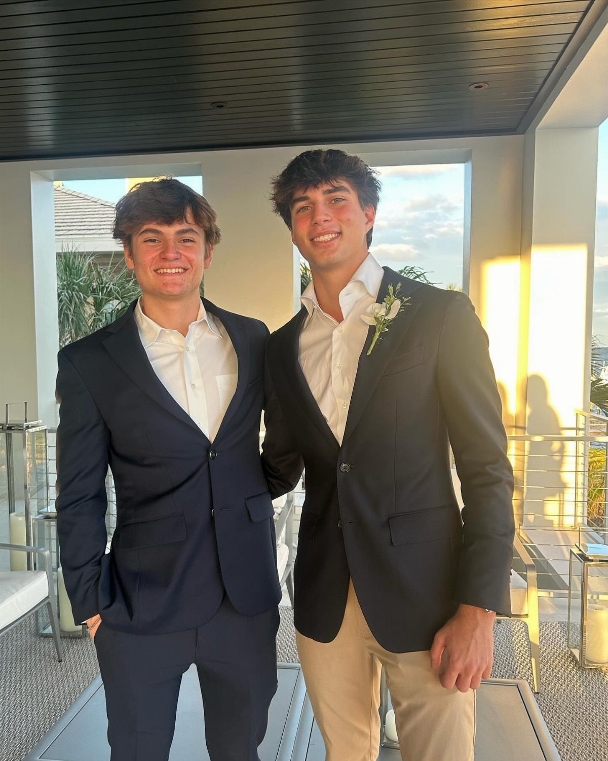 Two young men in semi-formal navy blazers and dress shirts posing on a balcony.
