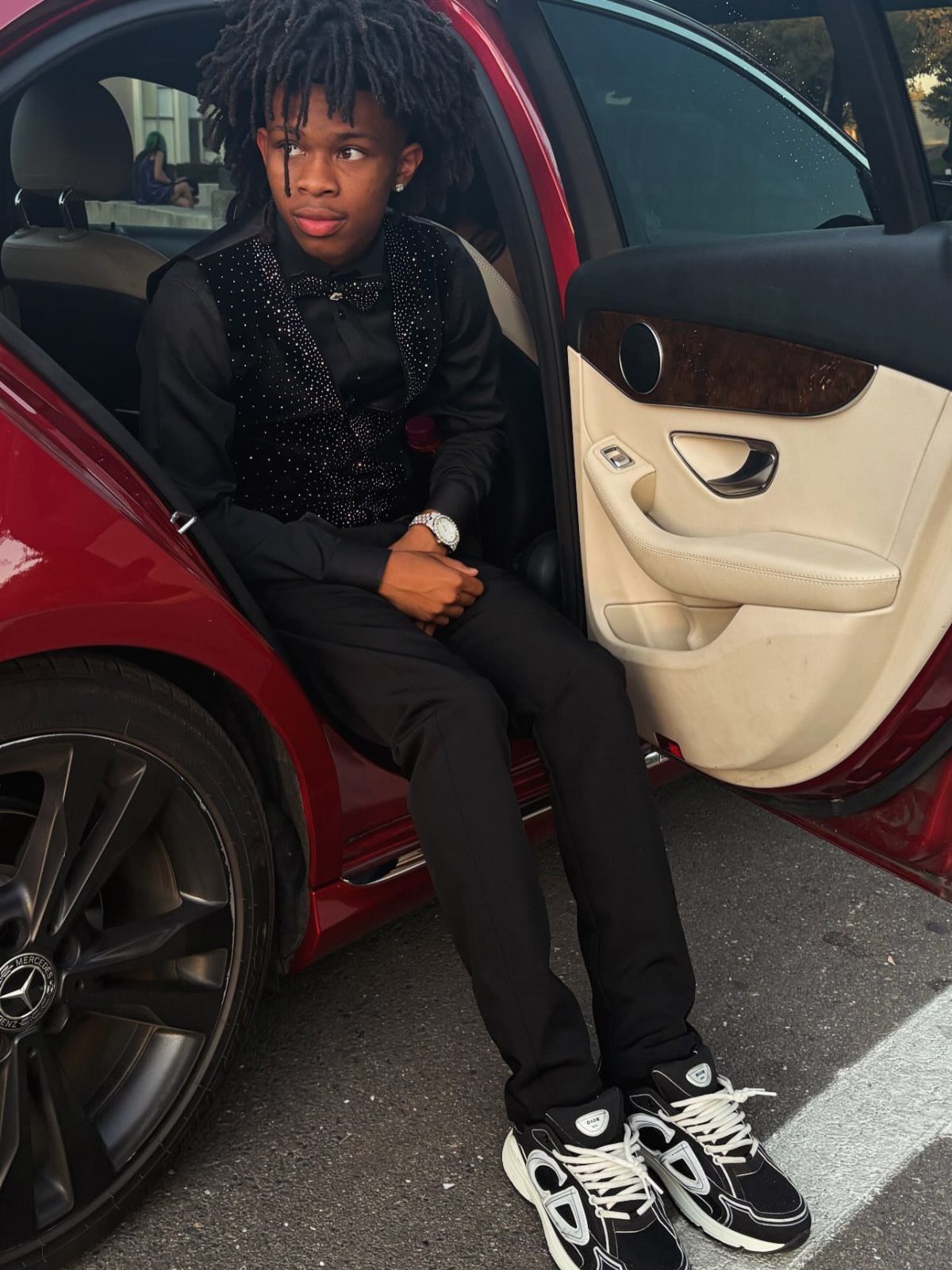 Young man in a sequined black vest and trousers sitting in a red car.