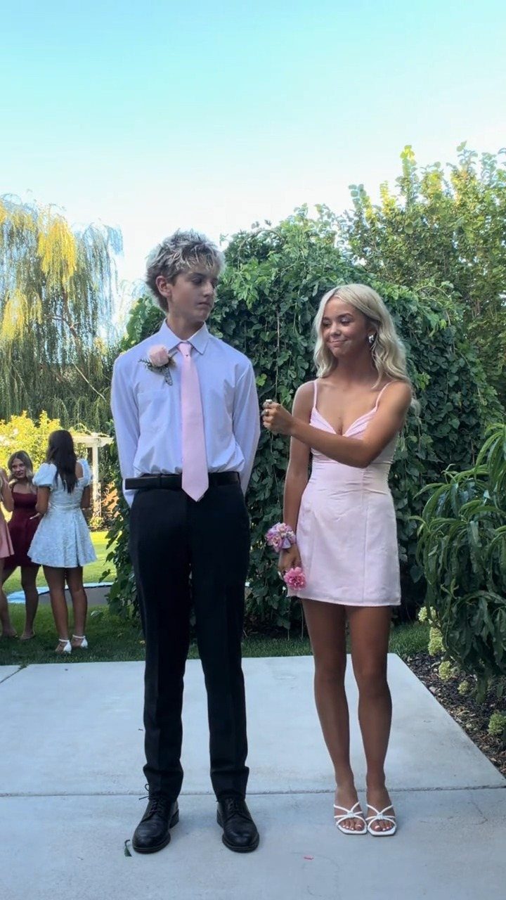 Young couple posing outdoors, man wearing a light pink tie and black belt.