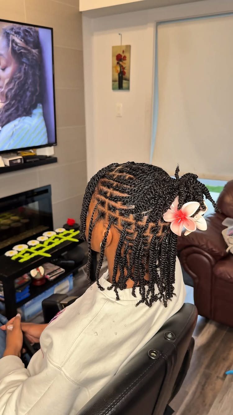 Short black braided hairstyle with a pink flower clip on a person.