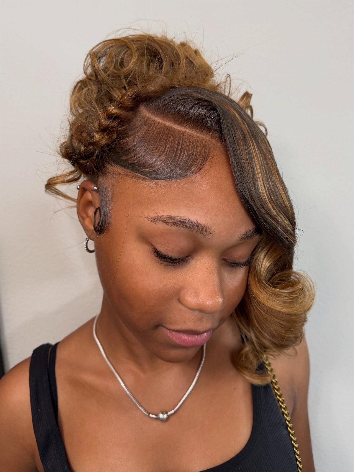 Woman with a high curly updo and side-swept blonde highlighted curls.
