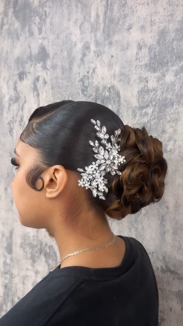 Sleek low curly updo with a silver rhinestone floral hair accessory on dark hair.