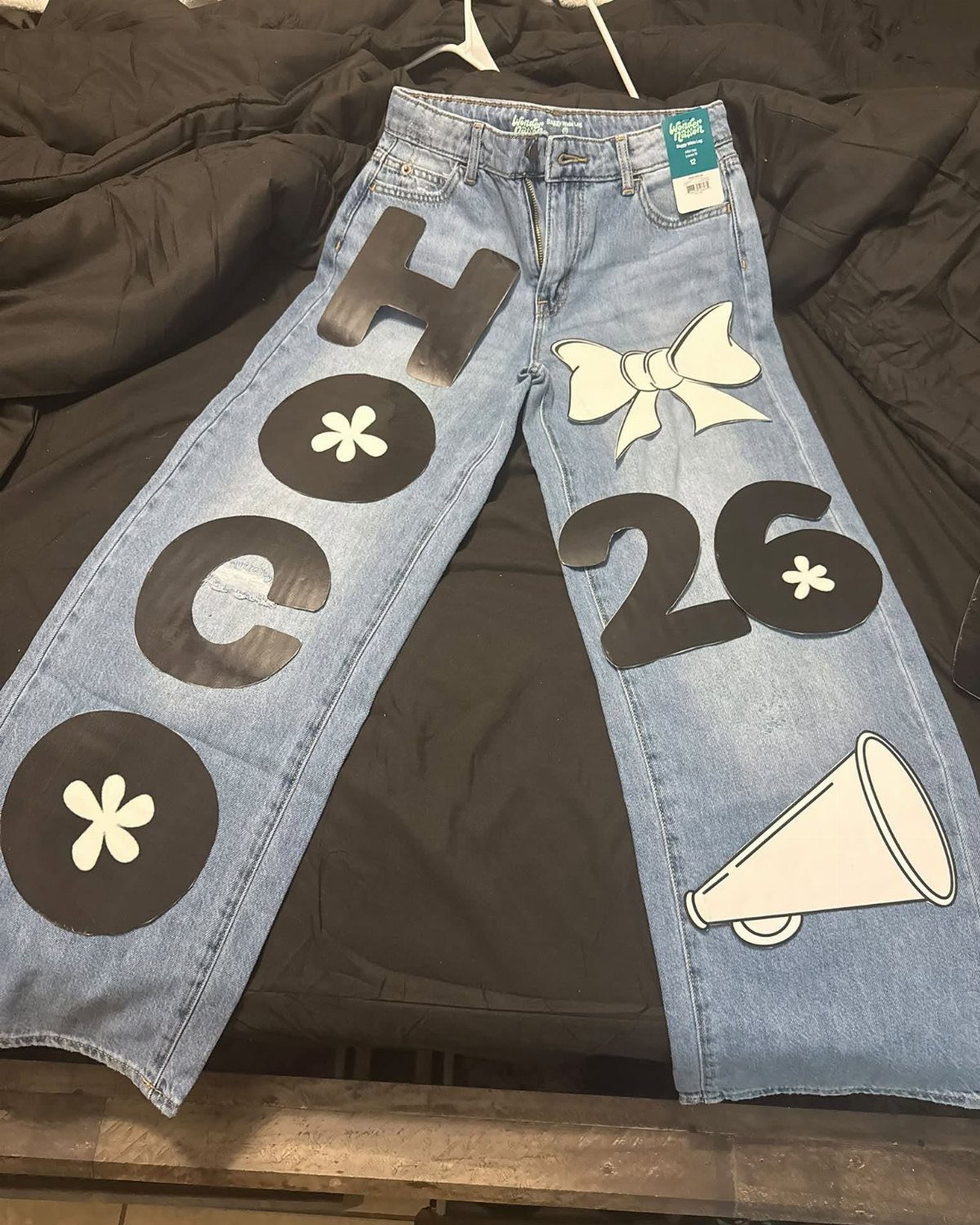 Light blue denim jeans decorated with black and white fabric patches and letters.