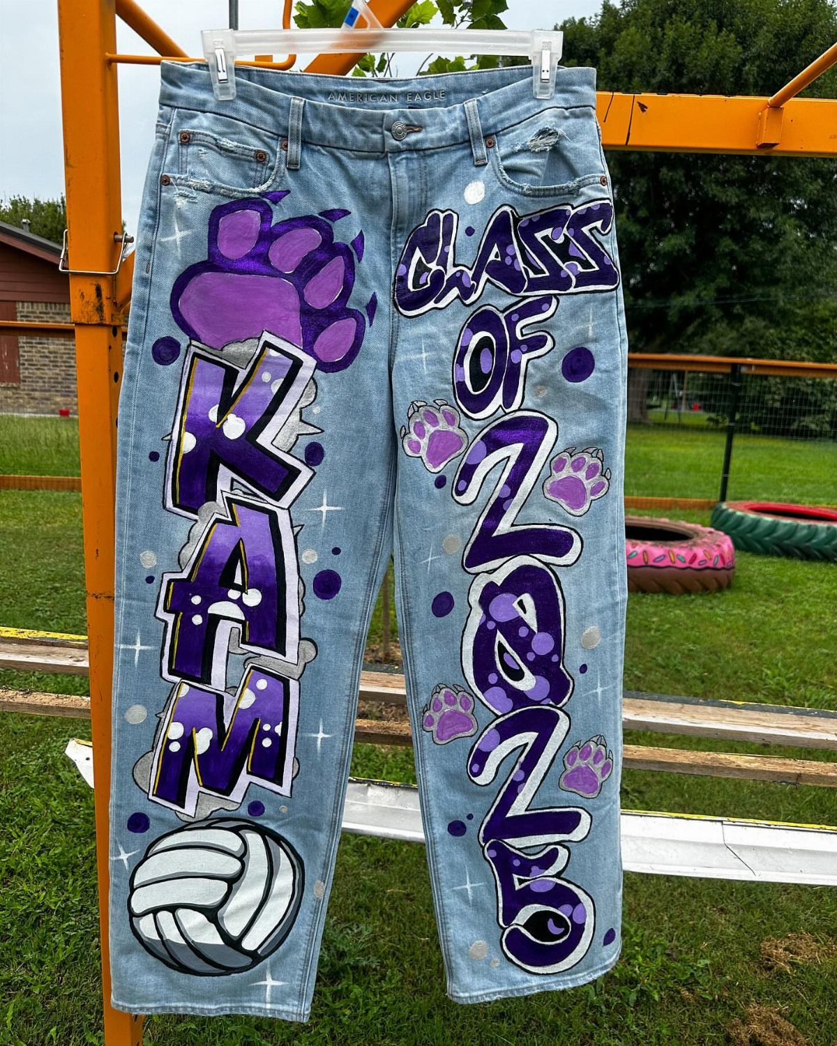 Hand painted light blue jeans featuring purple varsity text, paw prints, and a volleyball.