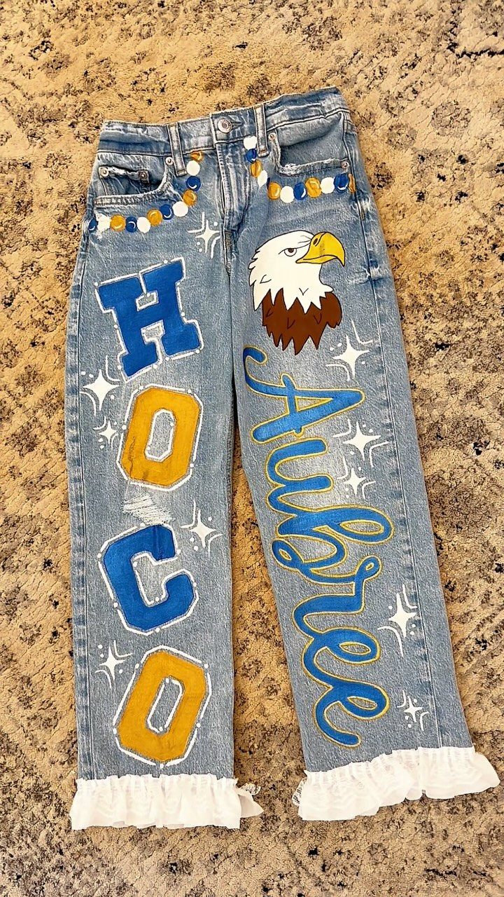 Light blue denim jeans decorated with HOCO letters, an eagle, and a name.