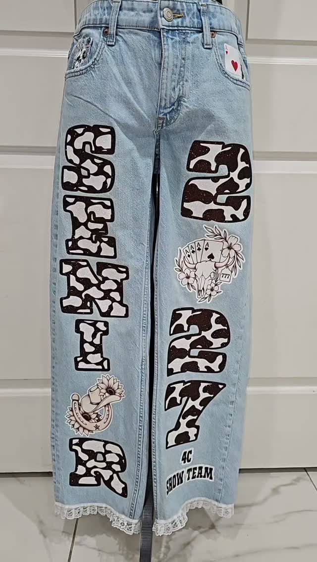 Light wash denim jeans with cow-print Senior 2017 letters and decorative patches.