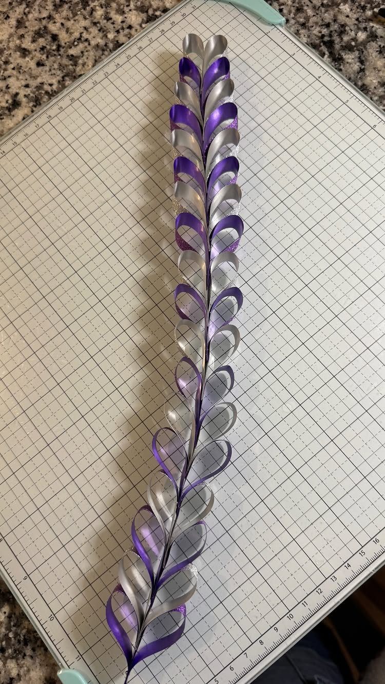 Purple and silver ribbon chain formed into interlocking heart shapes on a grid mat.