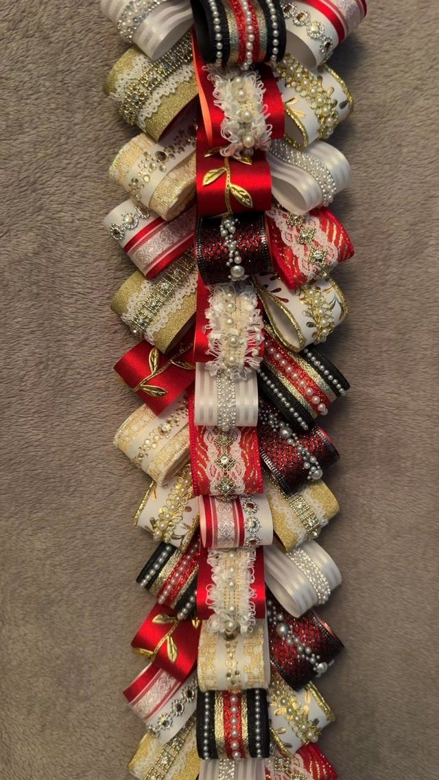 Braided homecoming mum accessory with red, white, and gold ribbons on beige carpet.
