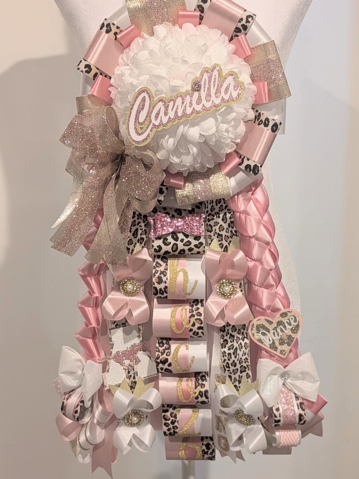 Homecoming mum with white pom-pom, pink ribbons, leopard print accents, and braided ribbons.