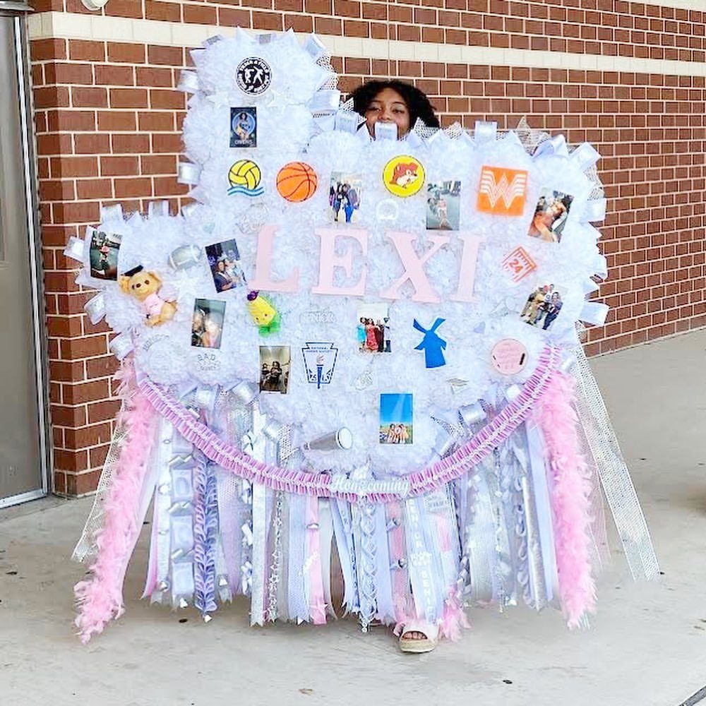 Enormous white homecoming mum with pink lettering and photos covering a person's torso.