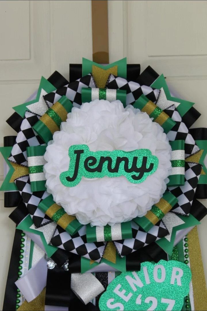 Personalized homecoming mum with white flower, green nameplate, and senior ribbons.