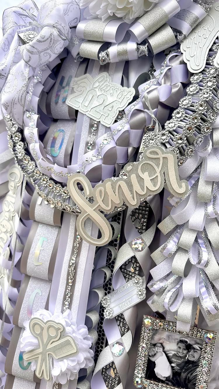 Silver and white senior homecoming mum with ribbons, charms, and a small photo.