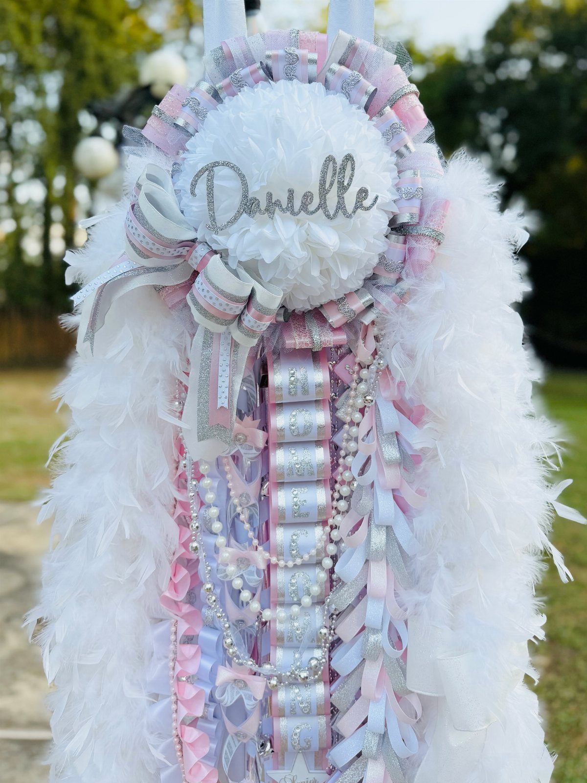 White and silver homecoming mum with pink accents, pearls, and fluffy white feathers.
