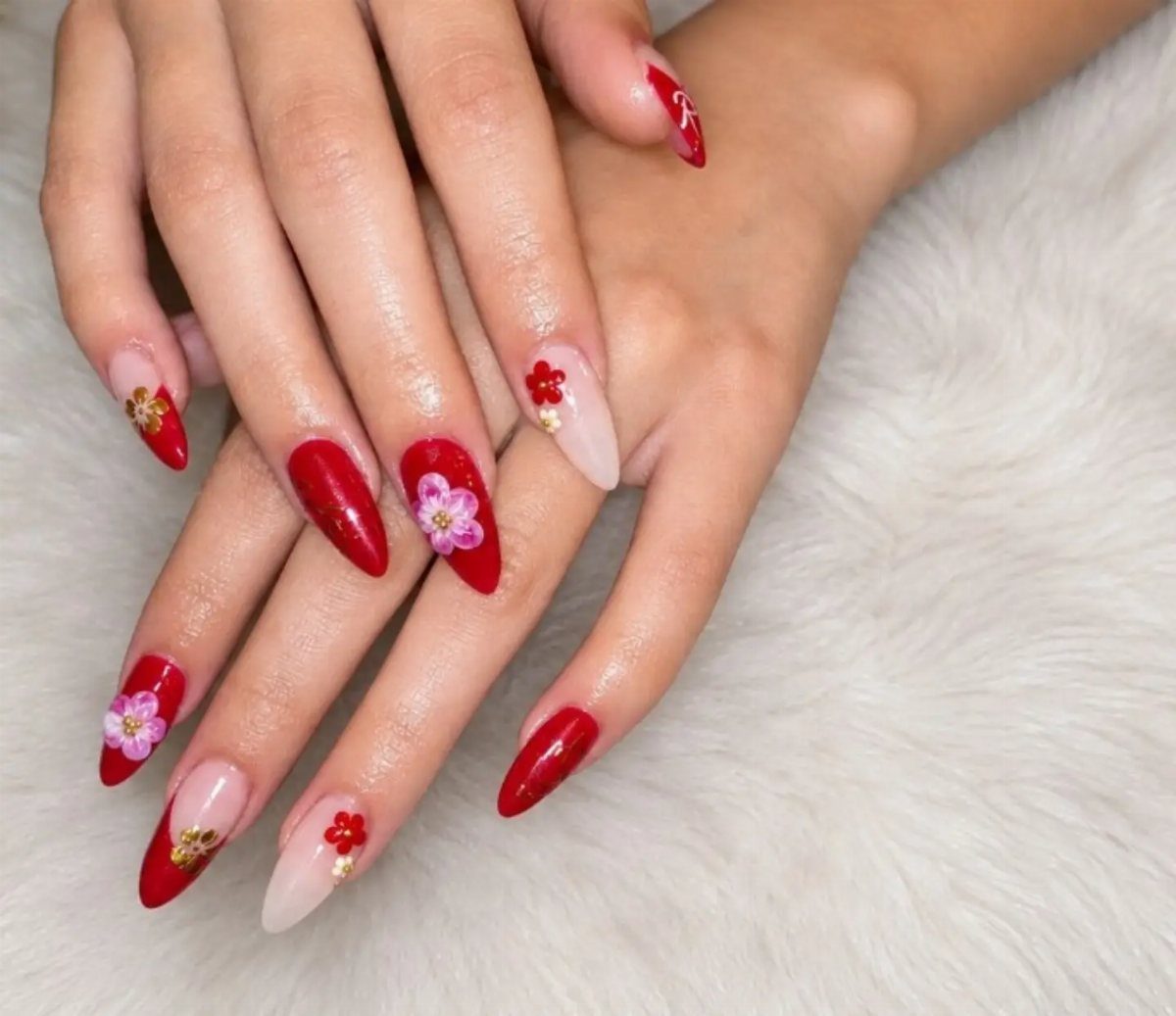 Almond-shaped nails with bold red polish and 3D floral nail art designs.