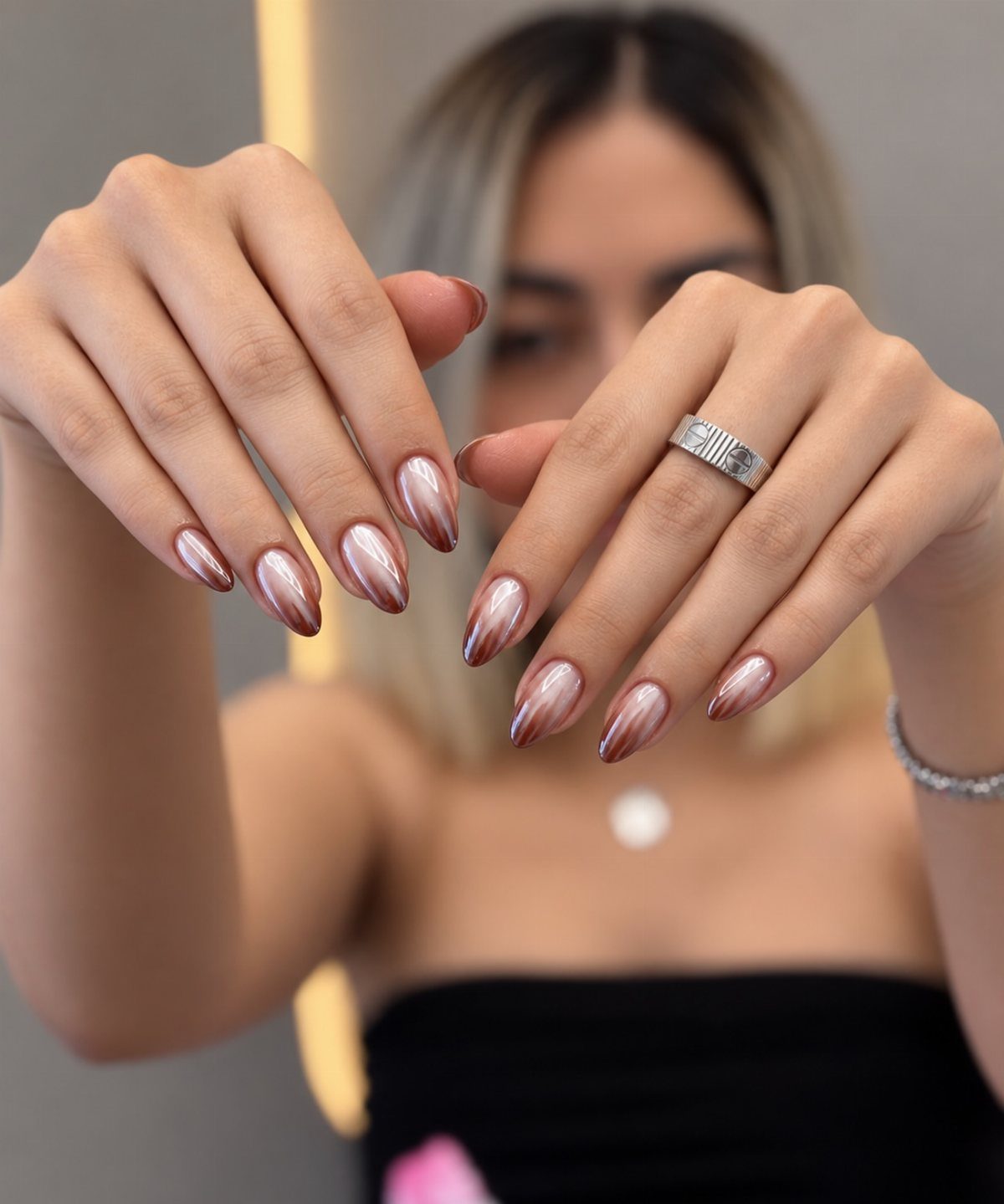 Almond-shaped nails with a shimmering metallic rose-gold chrome finish on a person's hands.