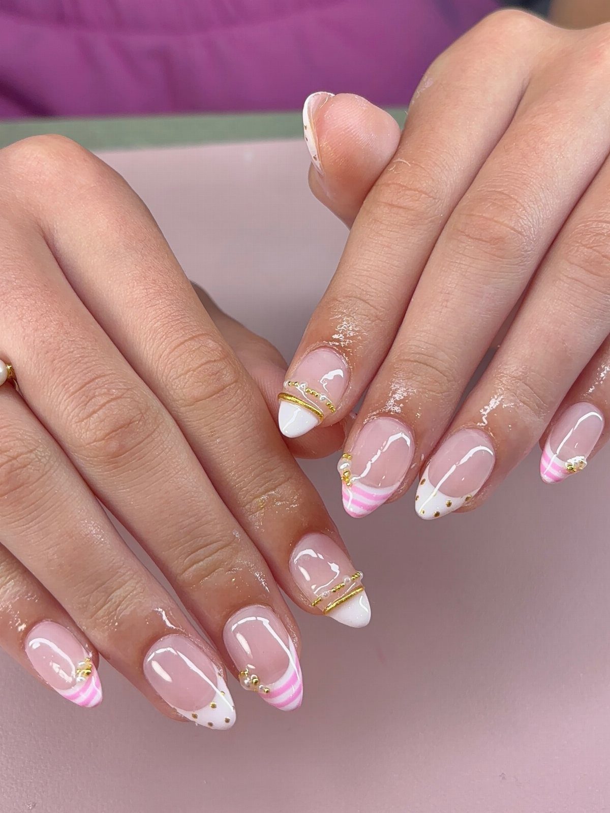 Almond-shaped nails with milky white and pink polish, gold bands, and glitter accents.