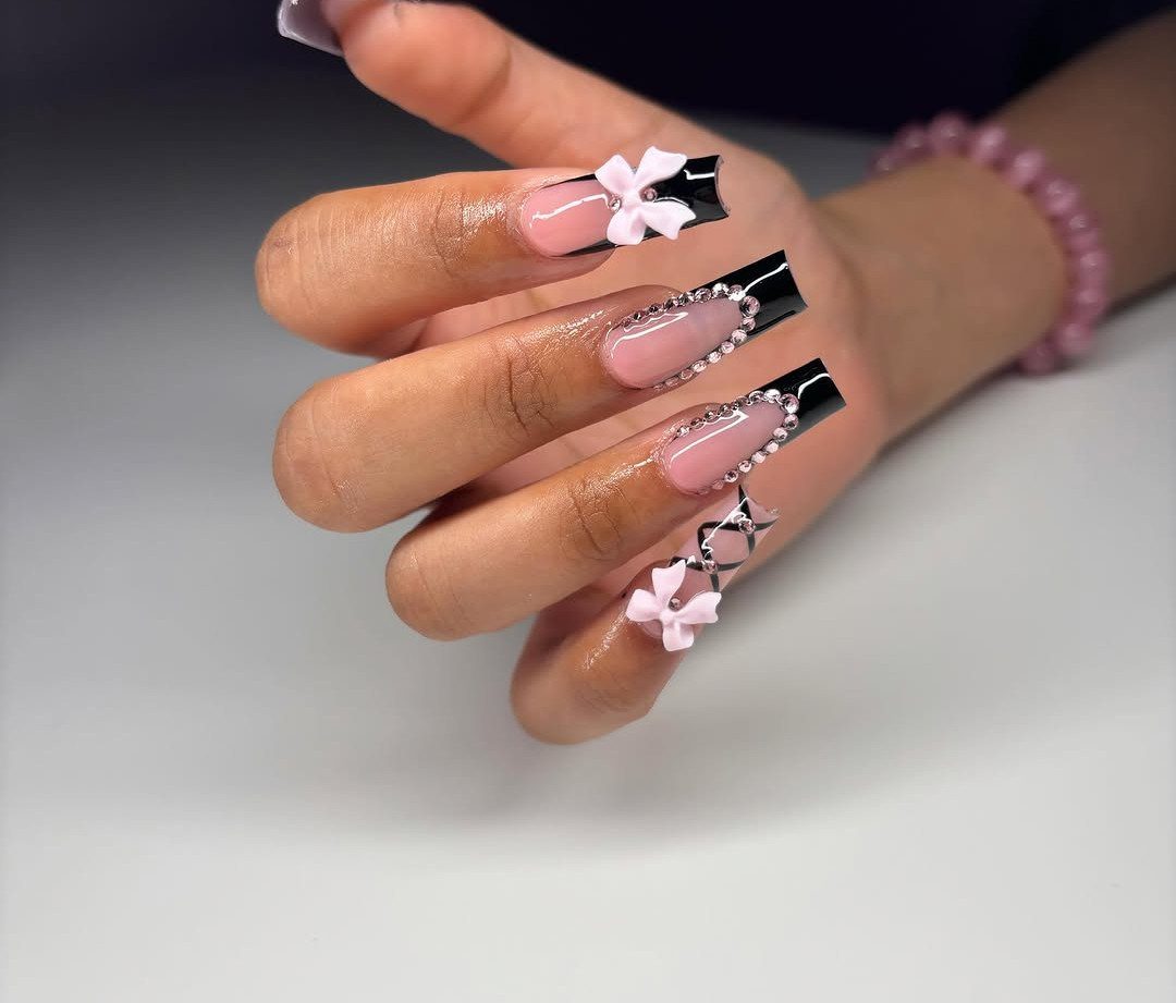 Long square nails with pink ombre, black tips, 3D bows, and silver rhinestones.