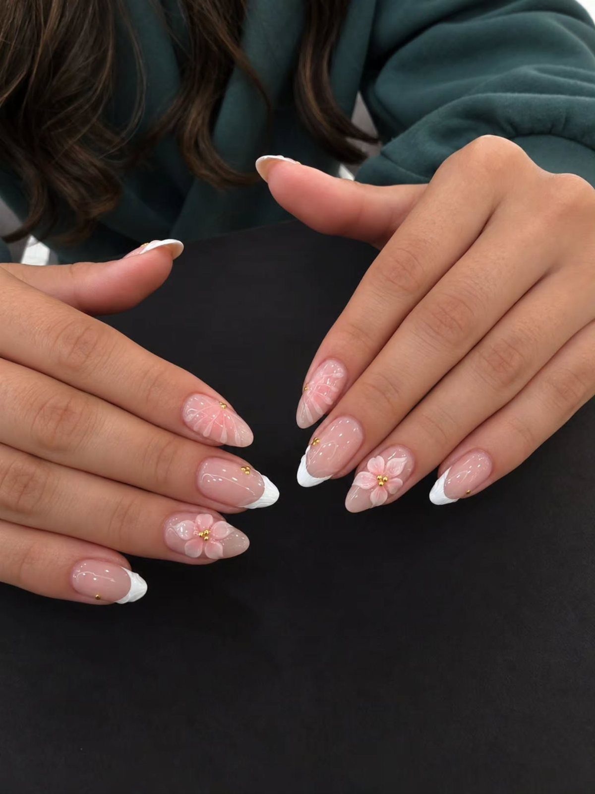Almond-shaped nails with pastel pink colors, white tips, and small 3D floral designs.