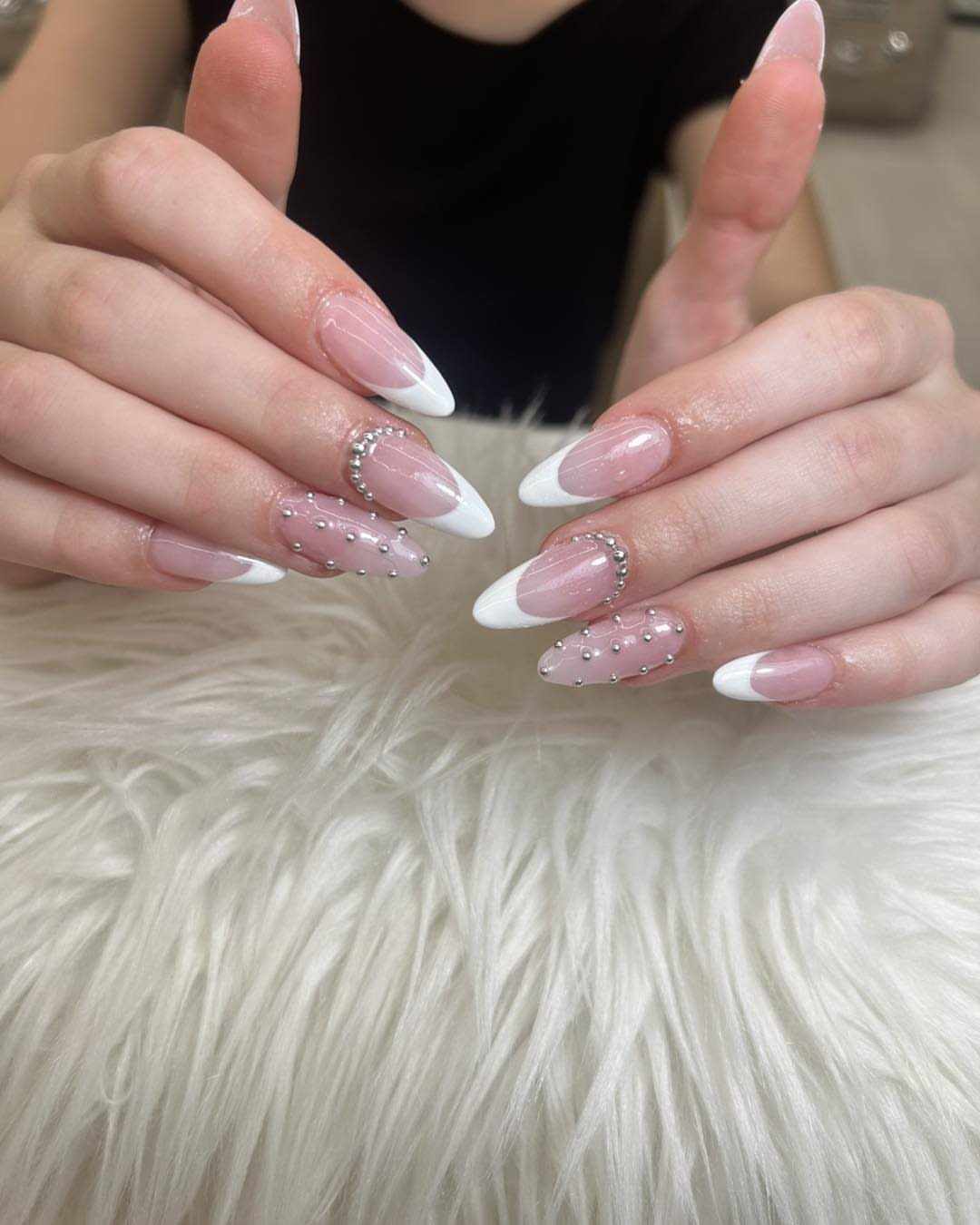 Almond-shaped French manicure nails with silver rhinestones resting on white faux fur.