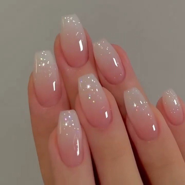 Almond-shaped nails with a nude ombre gradient and subtle shimmering glitter accents.